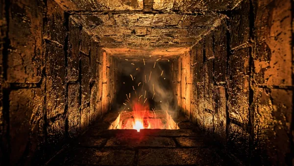 View up the inside of a masonry chimney flue with clay tiles coated in glossy black creosote tar, lit by a fierce orange fire glow and rising sparks from below — the start of a chimney fire.