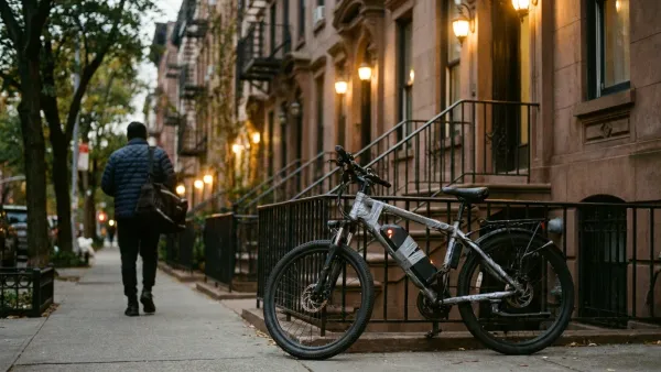 Wide overhead photograph at dusk of a low-rise New York City brownstone vestibule with a beat-up delivery e-bike leaning against the iron handrail of the front stoop; a single bright orange ember glows on the taped-up battery casing while a delivery rider in a quilted jacket walks past on the sidewalk — calm, unstaged street-level framing showing exactly where lithium-ion battery fires actually start, in residential entryways and stairwells of low-rise New York City buildings rather than open garages