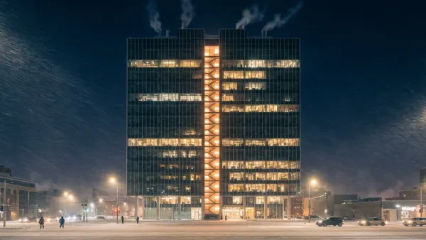 Wide cinematic cutaway photograph of a tall office tower at night under a deep-blue winter sky with snow blowing past lit windows; inside, a single illuminated emergency stairwell runs the full height of the building like a glowing vertical spine, with faint pale arrows of rising air suggesting stack effect drawing upward through the shaft — calm, architectural documentary framing that shows why a stairwell pressurization system behaves so differently on the coldest night of the year